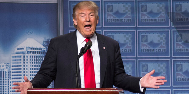 Trump an einem Rednerpult mit ausgebreiteten Armen Trump an einem Rednerpult mit ausgebreiteten Armen