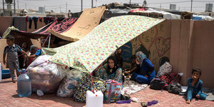 Menschen sitzen in einem Lager vor Zelten