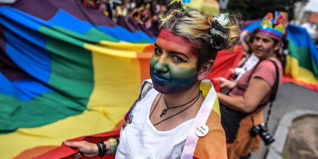 Eine Frau mit Regenbogenbemalung im Gesicht hält eine Regenbogenflagge Eine Frau mit Regenbogenbemalung im Gesicht hält eine Regenbogenflagge