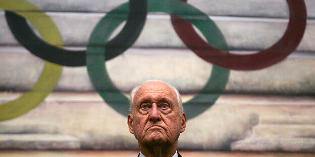 Kopf von Havelange am unteren Bildrand, mittig. Dahinter an der Wand die 5 olympischen Ringe Kopf von Havelange am unteren Bildrand, mittig. Dahinter an der Wand die 5 olympischen Ringe