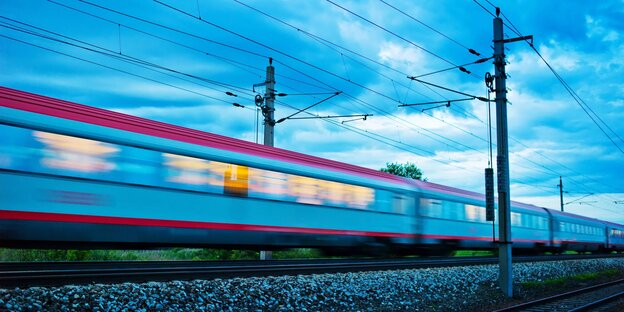 Ein Zug mit hellerleuchteten Fenstern fährt durch die Morgen- oder Abenddämmerung Ein Zug mit hellerleuchteten Fenstern fährt durch die Morgen- oder Abenddämmerung
