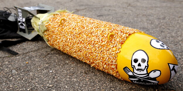 eine große mit Maiskörnern beklebte Bombenattrappe mit Monsanto-Totenkopf-Aufklebern eine große mit Maiskörnern beklebte Bombenattrappe mit Monsanto-Totenkopf-Aufklebern