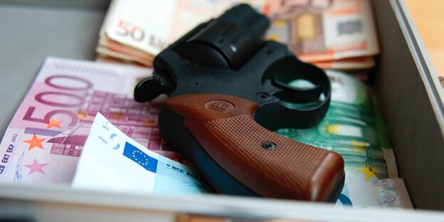 In einer Kasse liegt auf den Geldscheinen ein Revolver In einer Kasse liegt auf den Geldscheinen ein Revolver