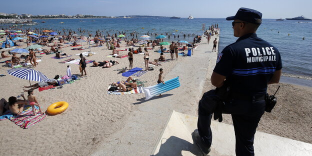 Ein uniformierter Polizist beobachtet den Strand von Cannes Ein uniformierter Polizist beobachtet den Strand von Cannes