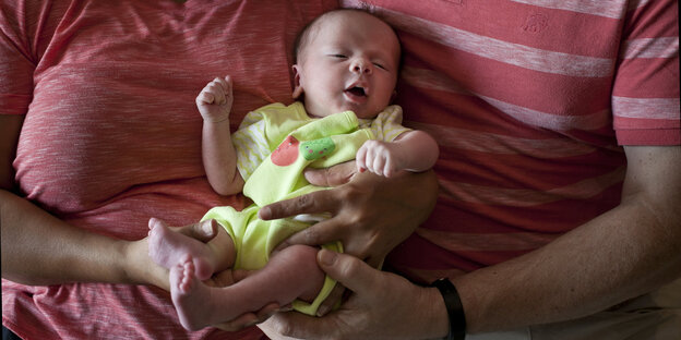 Ein sehr kleines Baby wird von Armen von Erwachsenen gehalten, deren Gesichter man nicht sieht Ein sehr kleines Baby wird von Armen von Erwachsenen gehalten, deren Gesichter man nicht sieht