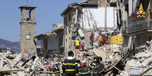 Feuerwehrleute in einer zerstörten Stadt, weiter hinten ein Kirchturm