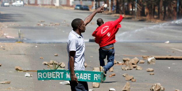 Ein Mann hält ein Schild mit der Aufschrift "Robert Mugabe Rd" und zeigt in die Ferne Ein Mann hält ein Schild mit der Aufschrift "Robert Mugabe Rd" und zeigt in die Ferne