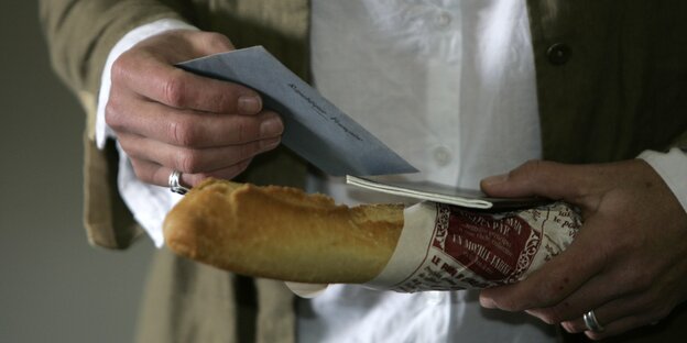 Ein Mensch hält ein Baguette und ein Papier in den Händen Ein Mensch hält ein Baguette und ein Papier in den Händen