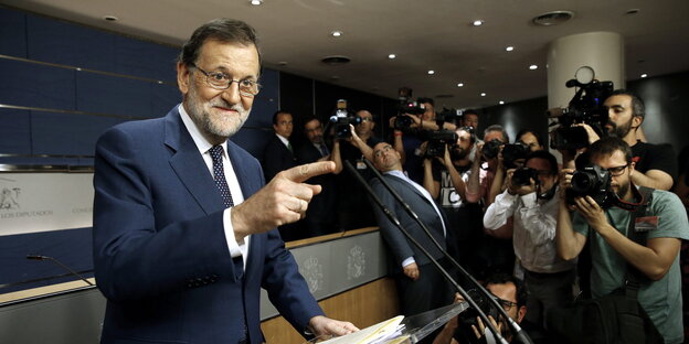 Rajoy lächelt und zeigt auf etwas bei einer Pressekonferenz, im Hintergrund viele FotografInnen Rajoy lächelt und zeigt auf etwas bei einer Pressekonferenz, im Hintergrund viele FotografInnen