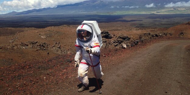 Eine Frau läuft im Astronautinnenanzug in einer bergigen Landschaft Eine Frau läuft im Astronautinnenanzug in einer bergigen Landschaft