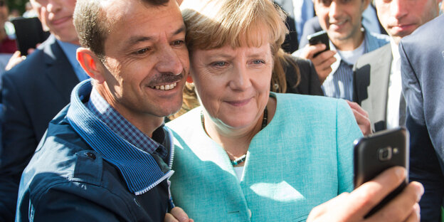 Ein Mann macht ein Selfie von sich und einer Frau in hellblauem Anzug Ein Mann macht ein Selfie von sich und einer Frau in hellblauem Anzug