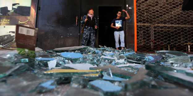 Zwei Männer stehen vor einem Gebäude, vor ihnen liegt zerbrochenes Glas