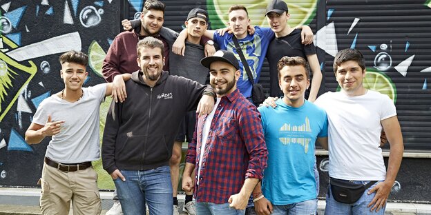 Jungs machen zusammen ein Gruppenbild, hinter ihnen ist ein Graffiti an die Wand gemalt Jungs machen zusammen ein Gruppenbild, hinter ihnen ist ein Graffiti an die Wand gemalt