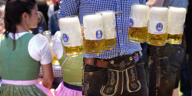 Ein Mann hat mehrere Bierkrüge in den Händen Ein Mann hat mehrere Bierkrüge in den Händen