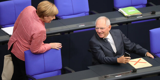 Ein Mann, rechts im Bild, sitzend, und eine Frau, links im Bild, stehend, sprechen miteinander