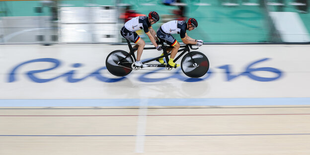 Ein Radsportler-Duo sprintet auf dem Tandem in einer Arena über den Bodenschriftzug Rio 2016 Ein Radsportler-Duo sprintet auf dem Tandem in einer Arena über den Bodenschriftzug Rio 2016