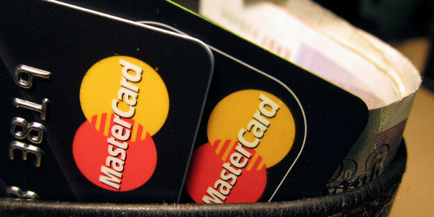 Zwei schwarze Mastercard-Kreditkarten mit rot-gelbem Logo stecken in einem Becher Zwei schwarze Mastercard-Kreditkarten mit rot-gelbem Logo stecken in einem Becher