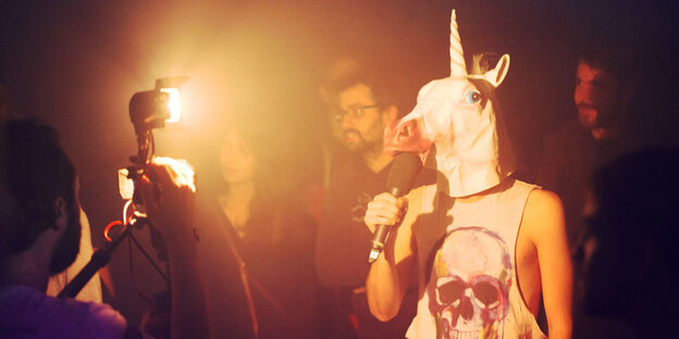 Schauspieler mit Einhornmaske spricht in ein Mikrofon Schauspieler mit Einhornmaske spricht in ein Mikrofon