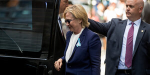 Hillary Clinton steigt in ein Auto ein, hinter ihr ein Mann in Anzug