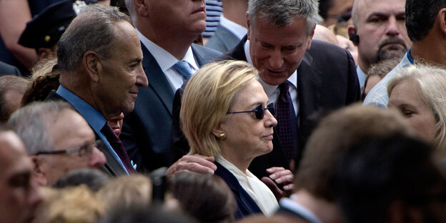 Hillary Clinton trägt eine schwarze Sonnenbrille und steht in einer Menschenmenge Hillary Clinton trägt eine schwarze Sonnenbrille und steht in einer Menschenmenge