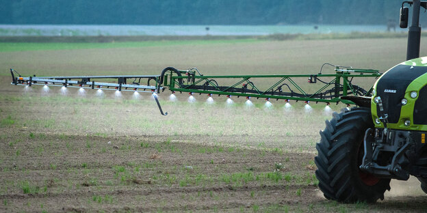 Ein Traktor fährt über ein Feld und versprüht über viele Düsen Pestizid Ein Traktor fährt über ein Feld und versprüht über viele Düsen Pestizid