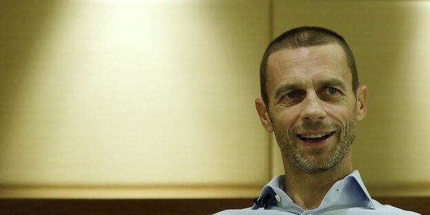 Aleksander Ceferin sitzt vor einer Wand und lacht Aleksander Ceferin sitzt vor einer Wand und lacht