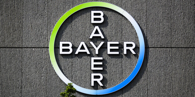 Vor dem Logo auf einer Wand der Firma Bayer wächst ein Baum Vor dem Logo auf einer Wand der Firma Bayer wächst ein Baum