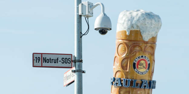 An einer Laterne hängt ein „Notruf“-Schild, daneben ragt ein künstlicher Bierkrug in die Höhe An einer Laterne hängt ein „Notruf“-Schild, daneben ragt ein künstlicher Bierkrug in die Höhe