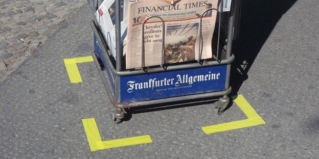 Ein zeitungssständer steht in einem mit gelben Klebeband abgeklebten Kästchen