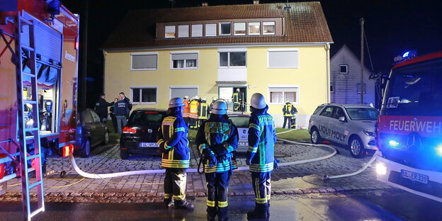 Feuerwehrmänner stehen vor einem Haus, links und rechts im Bild sind Feuerwehrfahrzeuge zu sehen Feuerwehrmänner stehen vor einem Haus, links und rechts im Bild sind Feuerwehrfahrzeuge zu sehen
