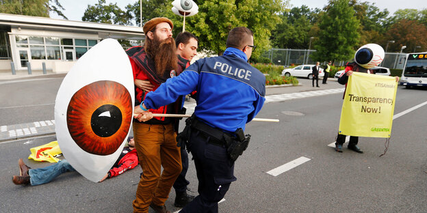 Ein Mann rangelt mit einem Polizisten um ein Pappmasché-Auge, das an einer Stange befestigt ist Ein Mann rangelt mit einem Polizisten um ein Pappmasché-Auge, das an einer Stange befestigt ist