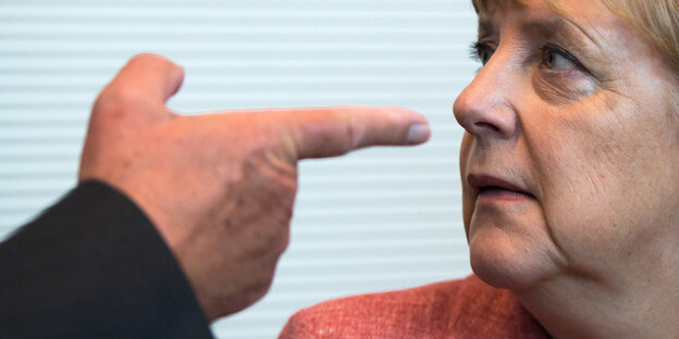Eine Hand zeigt mit dem Zeigefinger auf Angela Merkels Nase Eine Hand zeigt mit dem Zeigefinger auf Angela Merkels Nase