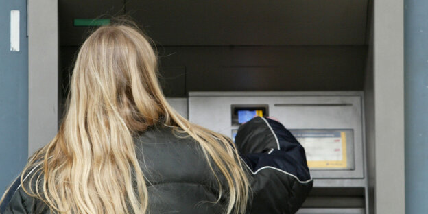 Eine Frau steht an einem Bankautomaten Eine Frau steht an einem Bankautomaten