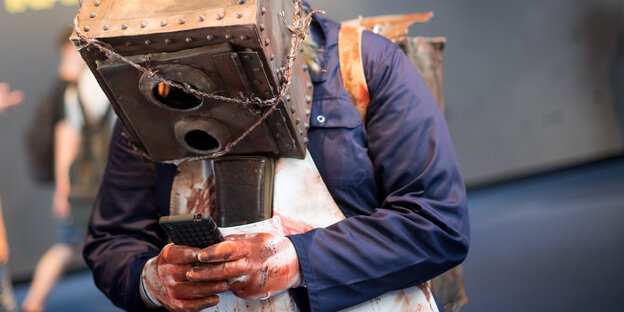 Eine person mit kastenförmiger Maske beugt sich über ihr Telefon Eine person mit kastenförmiger Maske beugt sich über ihr Telefon