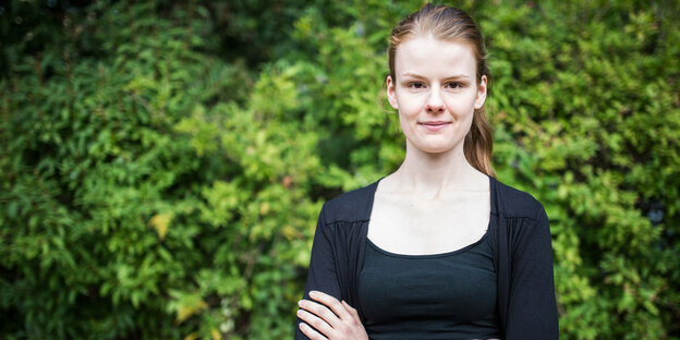 Jenna Behrens steht mit verschränkten Armen vor einer grünen Hecke Jenna Behrens steht mit verschränkten Armen vor einer grünen Hecke