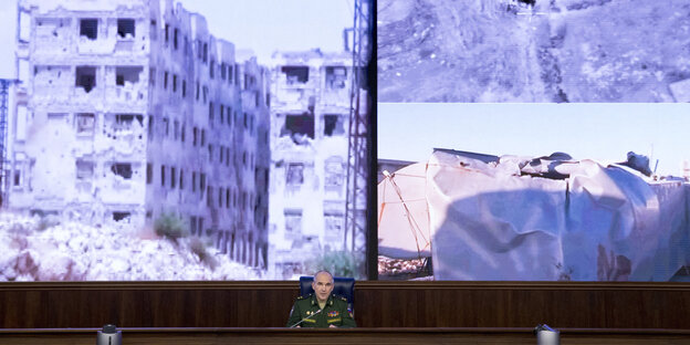 Der russische General Sergei Rudskoi vor einer riesigen Projektion von Aufnahmen zerstörter Häuser mutmaßlich in Syrien Der russische General Sergei Rudskoi vor einer riesigen Projektion von Aufnahmen zerstörter Häuser mutmaßlich in Syrien