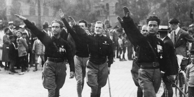 Männer in schwarzen Uniformen heben die rechte Hand zum fschistischen Gruß