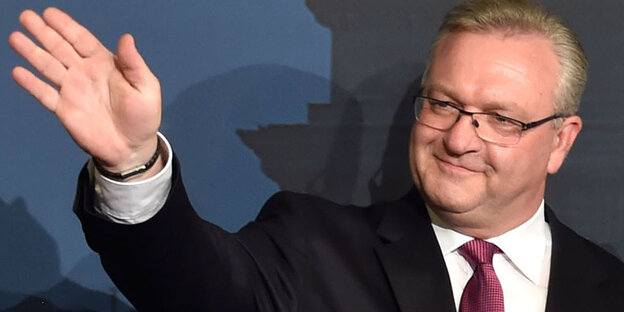 Ein älterer Mann mit Brille hält den Arm zum Winken hoch Ein älterer Mann mit Brille hält den Arm zum Winken hoch