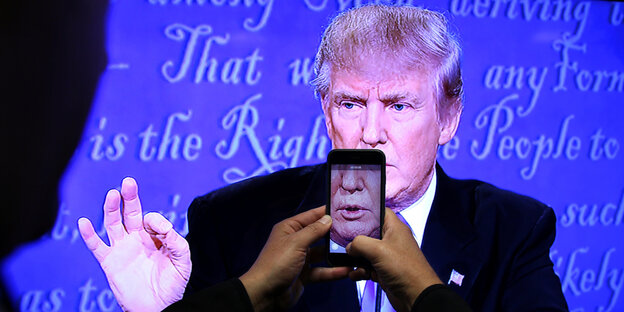 Ein Smartphone fotografiert Trumps Gesicht von einem Fernseher ab Ein Smartphone fotografiert Trumps Gesicht von einem Fernseher ab