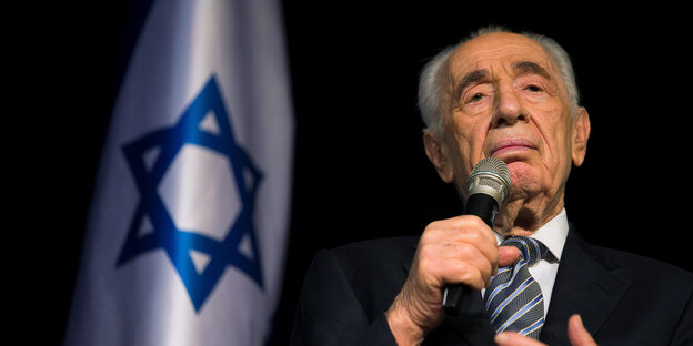 Peres mit Mikrofon im Porträt, daneben eine israelische Flagge Peres mit Mikrofon im Porträt, daneben eine israelische Flagge