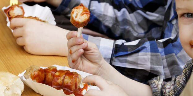 Ein Kind hält ein Stück Currywurst in die Höhe Ein Kind hält ein Stück Currywurst in die Höhe