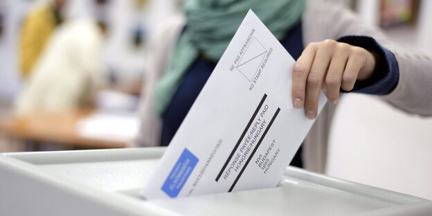 Eine Person wirft einen Stimmzettel in eine Wahlurne Eine Person wirft einen Stimmzettel in eine Wahlurne