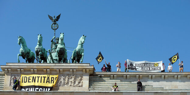 Männer protestieren mit Fahnen, auf denen "identitäre Bewegung", auf dem Brandenburger Tor Männer protestieren mit Fahnen, auf denen "identitäre Bewegung", auf dem Brandenburger Tor