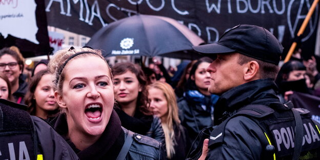 Eine Frau schreit, neben ihr steht ein Polizist, dahinter eine Menschenmenge Eine Frau schreit, neben ihr steht ein Polizist, dahinter eine Menschenmenge