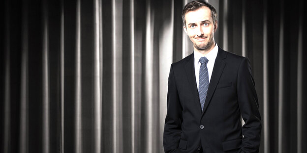 Jan Böhmermann vor grau-schwarzem Vorhang blickt in die Kamera Jan Böhmermann vor grau-schwarzem Vorhang blickt in die Kamera