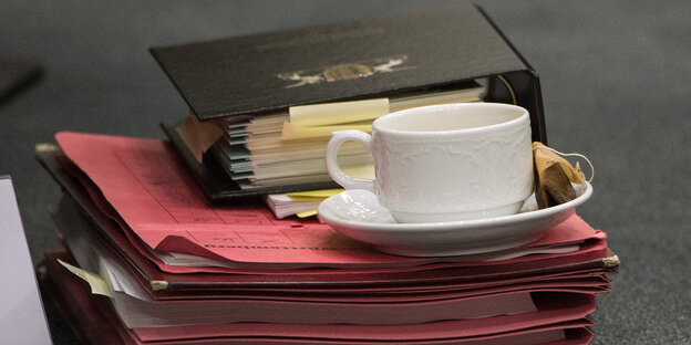 Ein Stapel roter Aktenmappen, darauf ein Aktenordner und eine Tasse auf Untertasse Ein Stapel roter Aktenmappen, darauf ein Aktenordner und eine Tasse auf Untertasse