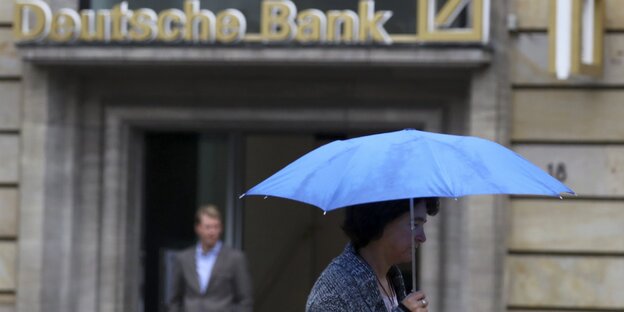 Eine Frau mit Regenschirm läuft an einer Filiale der Deutschen Bank vorbei. Eine Frau mit Regenschirm läuft an einer Filiale der Deutschen Bank vorbei.