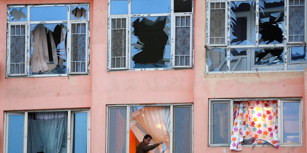 Sechs Fenster mit zetrümmertem Glas, aus einem weht eine bunte Gardine Sechs Fenster mit zetrümmertem Glas, aus einem weht eine bunte Gardine