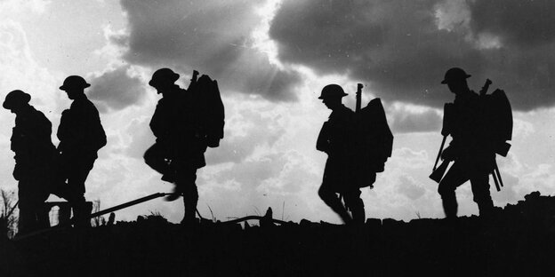 Die im Gegenlicht fotografierten Silhouetten von fünf gehenden Soldaten mit Gepäck Die im Gegenlicht fotografierten Silhouetten von fünf gehenden Soldaten mit Gepäck