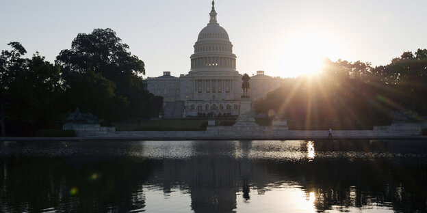 Hinter dem Capitol in Washington geht die Sonne auf, das Gebäude spiegelt sich im Wasser Hinter dem Capitol in Washington geht die Sonne auf, das Gebäude spiegelt sich im Wasser